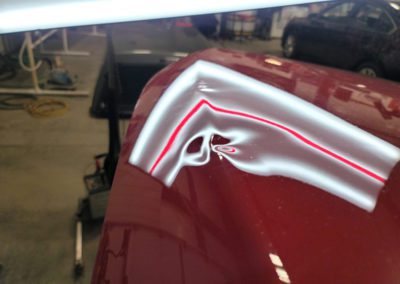 Hood of a red car with a small dent brought to MBT INC DBA Cheyenne Ding Guy.